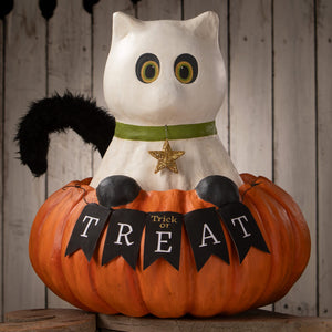 White papier-mâché casper cat with yellow eyes and green collar sitting on orange pumpkin with trick or treat flags for halloween cats
