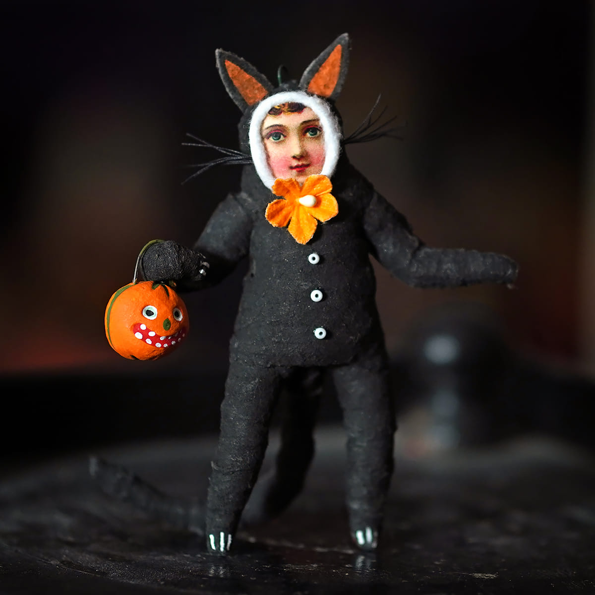 Trick or treat cat child figure dressed in textured black outfit with orange tipped ears and matching flower bow