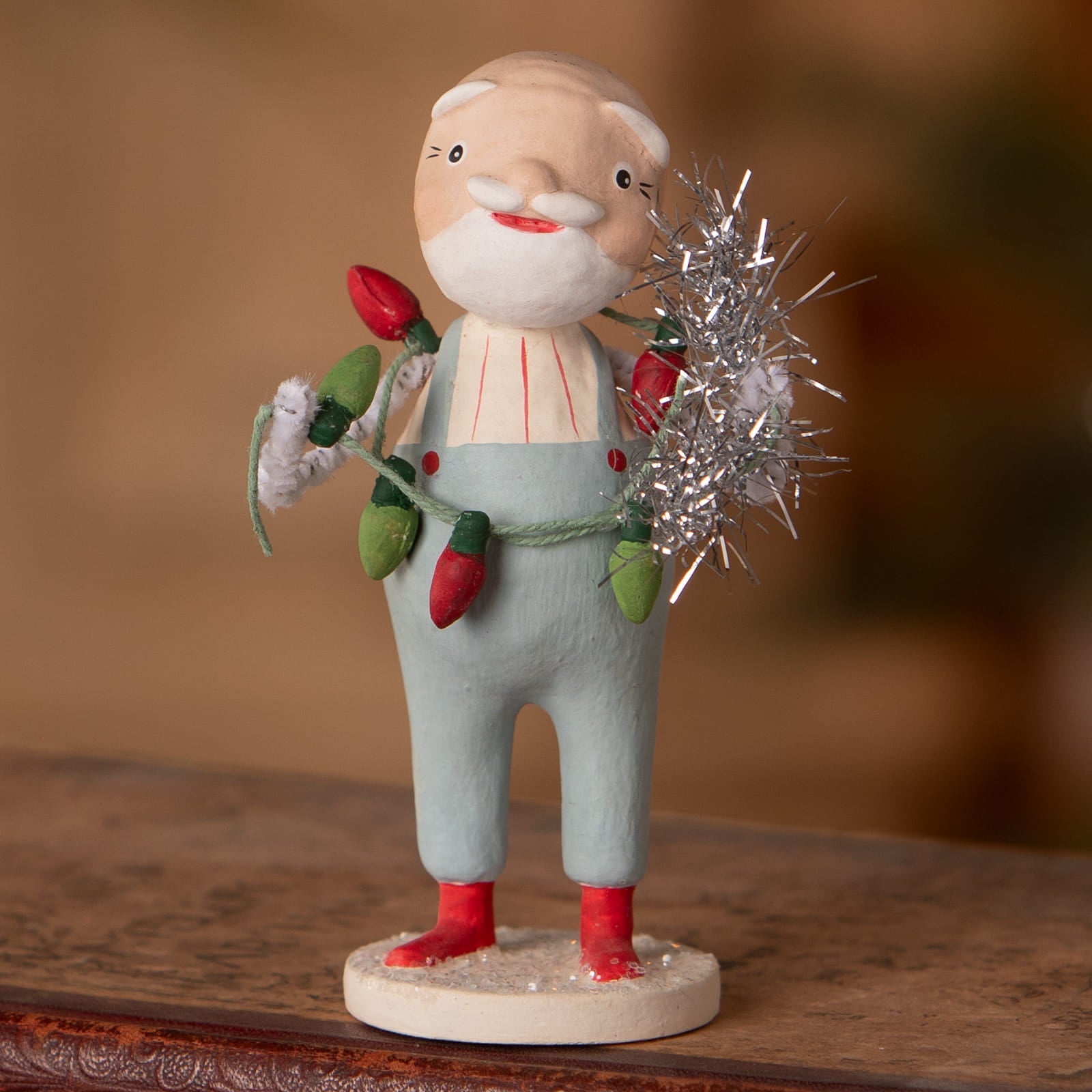 A charming hand-painted trim the tree santa figurine in light blue overalls holding christmas lights by bethany lowe designs