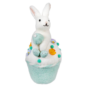 A bath bomb decorated with a white bunny, speckled eggs, and colorful flower accents.