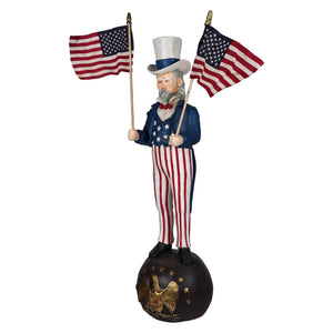 A painted wooden bethany lowe design uncle sam stands holding two american flags atop an eagle globe ball