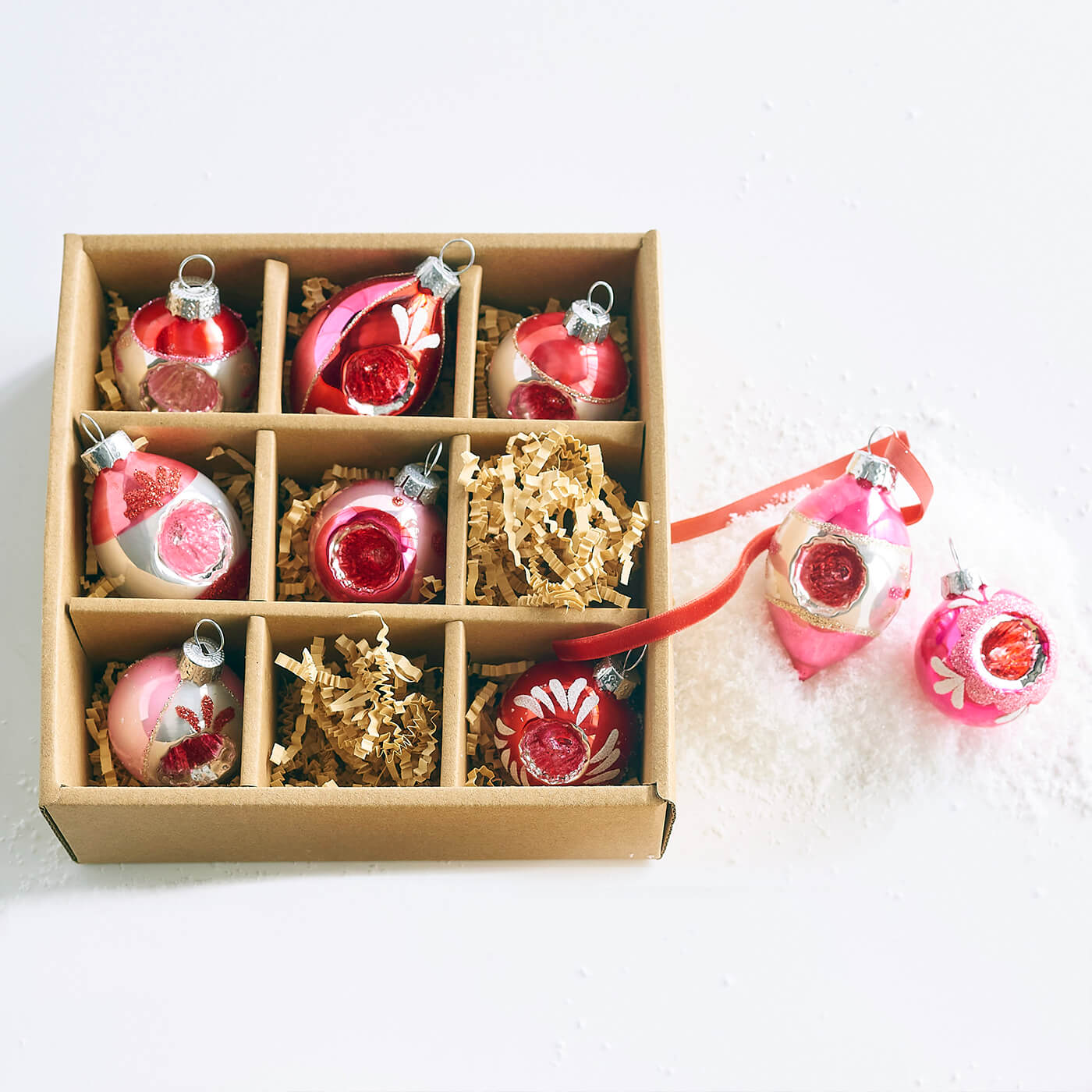 Box of vintage-style pink and red Christmas ornaments with some loose ornaments beside it.