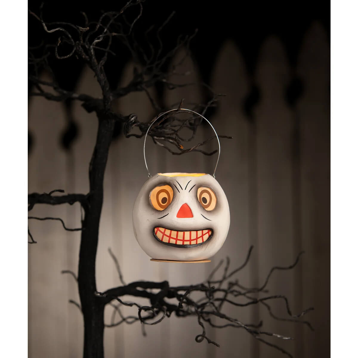 A white ceramic vintage skeleton bucket halloween lantern with a spooky smiling face and orange eyes and nose