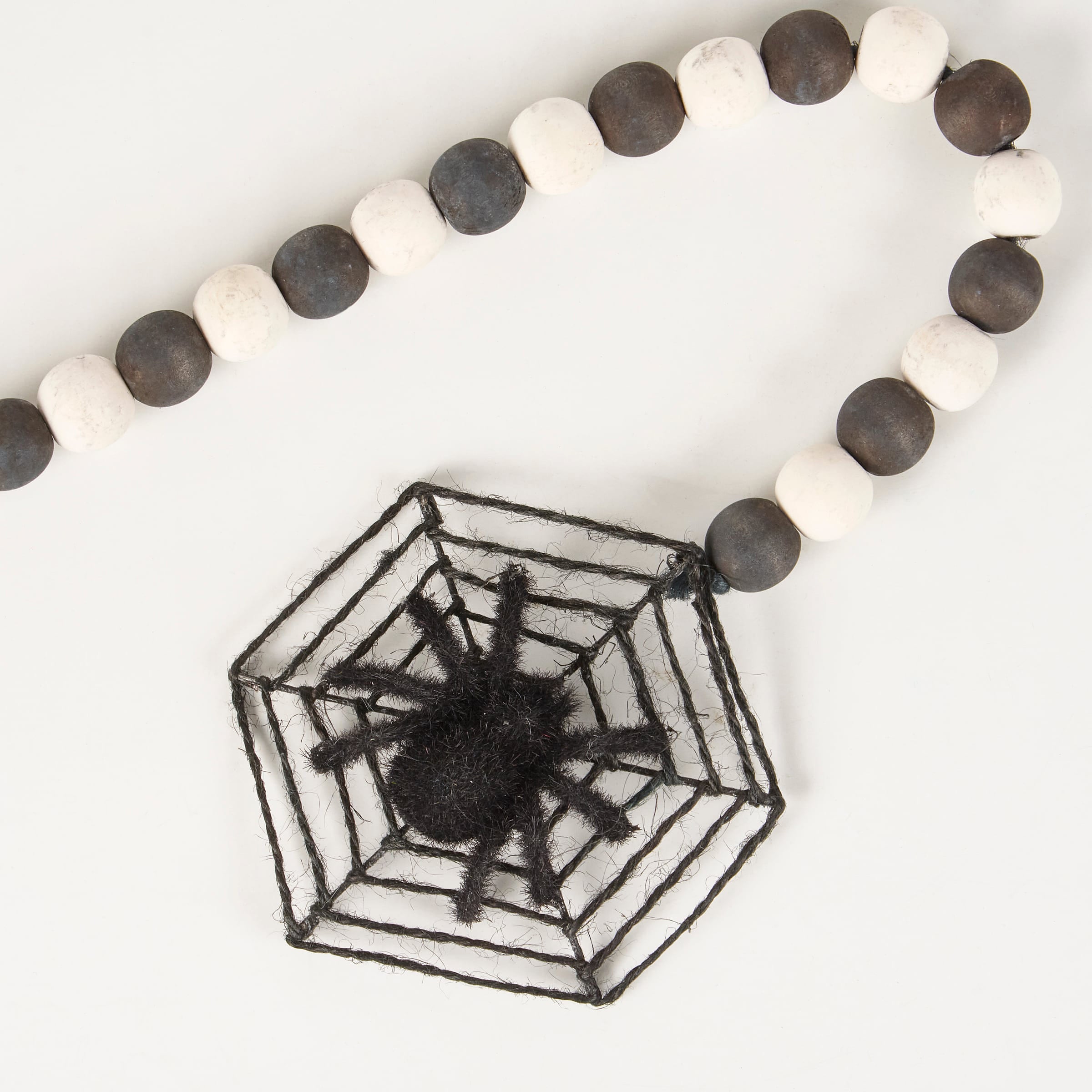 Black fuzzy spider centered in a hexagonal black yarn web on a black rings garland with alternating black and white beads