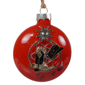 Red glass ball christmas ornament featuring a silver sun with a black cowboy boot and hat with gold accents