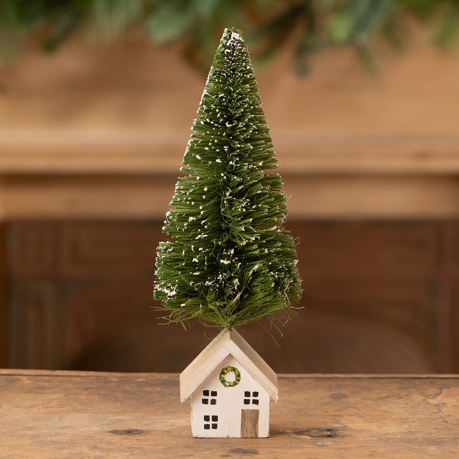 A miniature green bottle brush tree with white snow accents on a rustic wooden house vintage christmas village tree