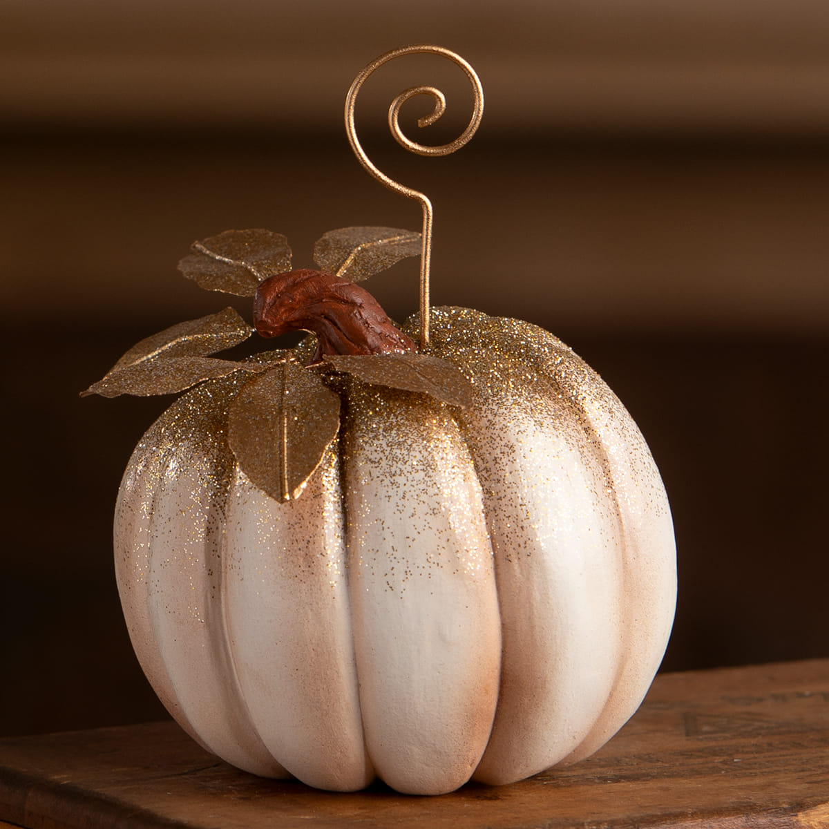 A glittery white pumpkin placecard holder with gold leaf accents and a metallic stem perfect for halloween pumpkins and gourds decor
