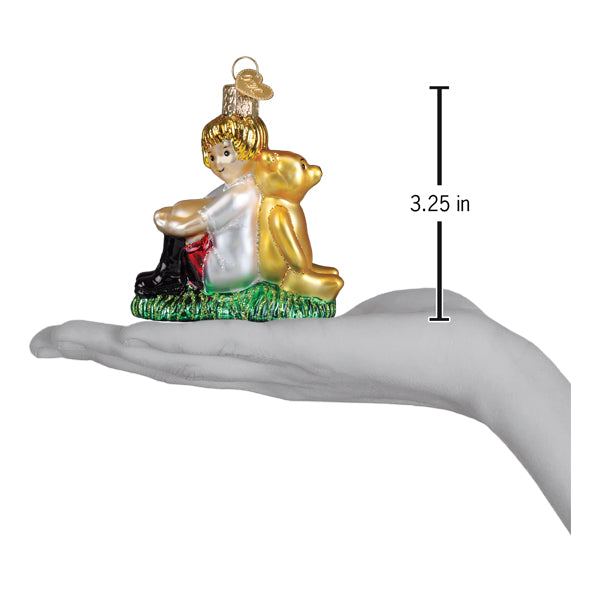 A golden glass christopher robin ornament with a child in white sitting with winnie the pooh on green grass