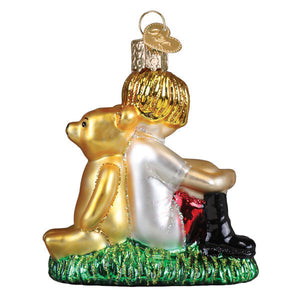 Golden glass christopher robin ornament showing child in white dress with black boots hugging golden bear on green grass