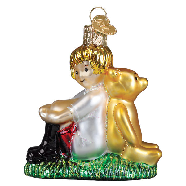 A golden glass christopher robin ornament with a blonde child in white dress sitting by a gold teddy on green grass
