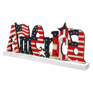 Decorative wooden ’America’ text sign painted with American flag stars and stripes pattern.