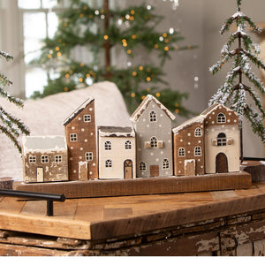 A wooden village set with five hand-painted vintage reproduction christmas village houses in earthy tones and snow-dusted roofs