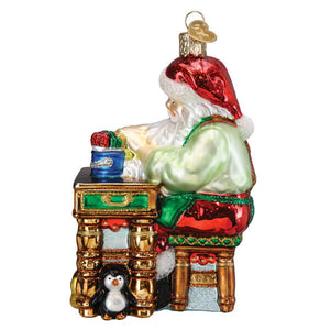 Glass workshop santa ornament with red hat green coat red pants seated at gold desk with penguin christmas glass ornament