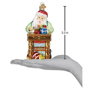 Glass workshop santa ornament with red hat white beard green coat seated on golden fireplace mantel christmas glass ornament