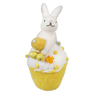 A white bunny sitting atop a yellow bath bomb decorated with flowers and bubbles.